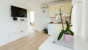 Una sala de estar moderna con una televisión de pantalla plana, una planta en maceta y una zona de comedor con mesa y sillas.