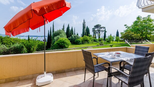 Una terraza con mesa y sillas, una sombrilla roja, y vistas a un paisaje verde y árboles.