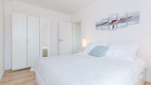 Un dormitorio con una cama grande, paredes blancas, un armario blanco y una obra de arte abstracto colgada en la pared.