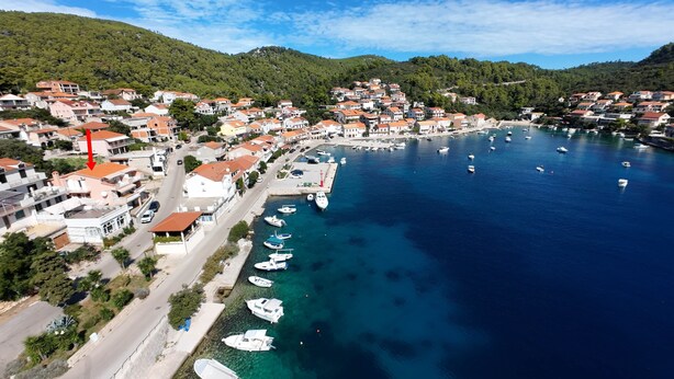 An aerial view of a coastal town with residential buildings, a marina, and boats docked along the waterfront.