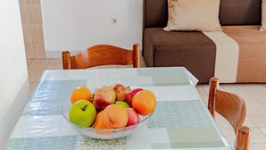 A dining table with a fruit bowl, a brown sofa, and a wooden chair in a room with a tiled floor.