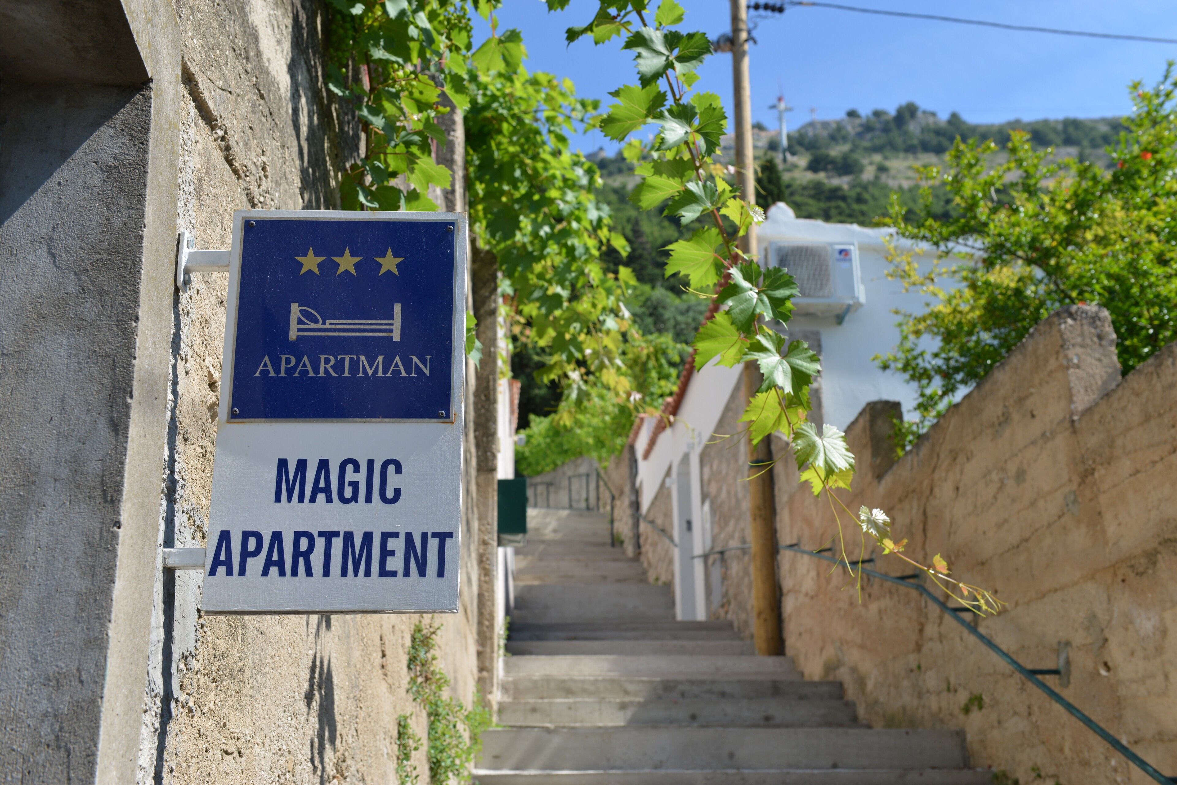 Un letrero indica un edificio con el nombre 'MAGIC APARTMENT' y una escalera que lleva a la entrada.