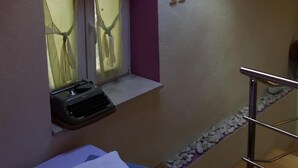 A small room with a skylight, a window with curtains, a small desk with a keyboard, a bed with pillows, and a wooden floor. - Apartments Elena (ST) - Duplex Studio Apartment (Purple) (Split)