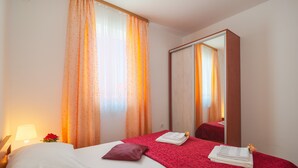 A hotel room with a bed, a mirror, a nightstand with a lamp, and a window with curtains. - Apartments Island Beat - Two Bedroom Apartment with Balcony and Sea View (A2) (ST) (Supetar)