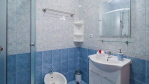 A bathroom with a glass shower enclosure, a white sink with a mirror above it, and blue-tiled walls. - Apartments Island Beat - Two Bedroom Apartment with Balcony and Sea View (A2) (ST) (Supetar)