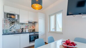 A modern kitchen with white cabinets, a microwave, and a stove. There is a dining table with a basket of pomegranates. - Villa Stella - Two Bedroom Apartment with Terrace and Sea View (Stella) (Splitska)