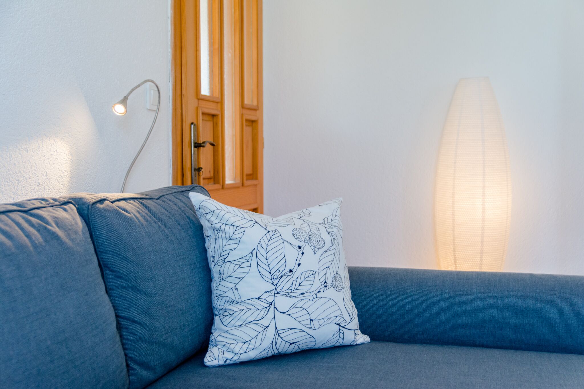 A modern living room with a blue sofa, a patterned throw pillow, a floor lamp, and a window with wooden frames.