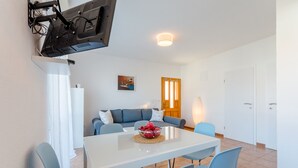 A modern living room with a white dining table, blue chairs, a blue sofa, and a TV mounted on the wall. - Villa Stella - Two Bedroom Apartment with Terrace and Sea View (Stella) (Splitska)