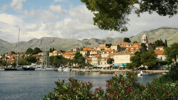Eine Küstenstadt mit Gebäuden an der Uferlinie, Booten im Hafen und Bergen im Hintergrund.