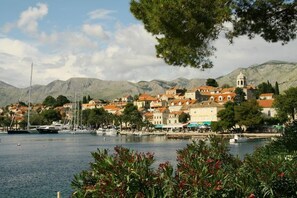 Una cittadina costiera con edifici lungo il lungomare, barche ormeggiate e montagne sullo sfondo.
