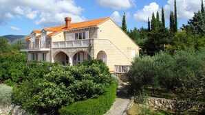 Ein großes, zweistöckiges Haus mit rotem Ziegeldach, umgeben von üppiger Vegetation und Bäumen.