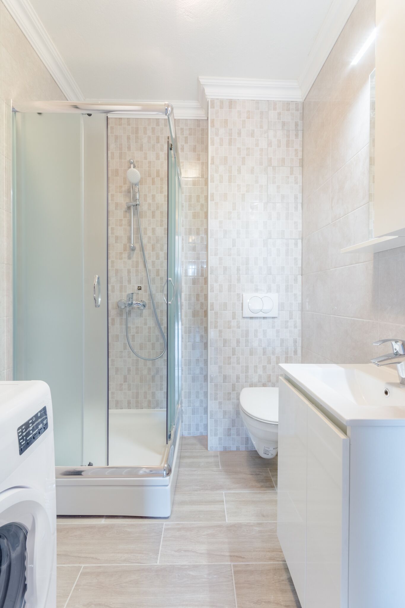 Une salle de bain moderne dotée d’une douche à parois de verre, de toilettes et d’un lave-linge encastré.