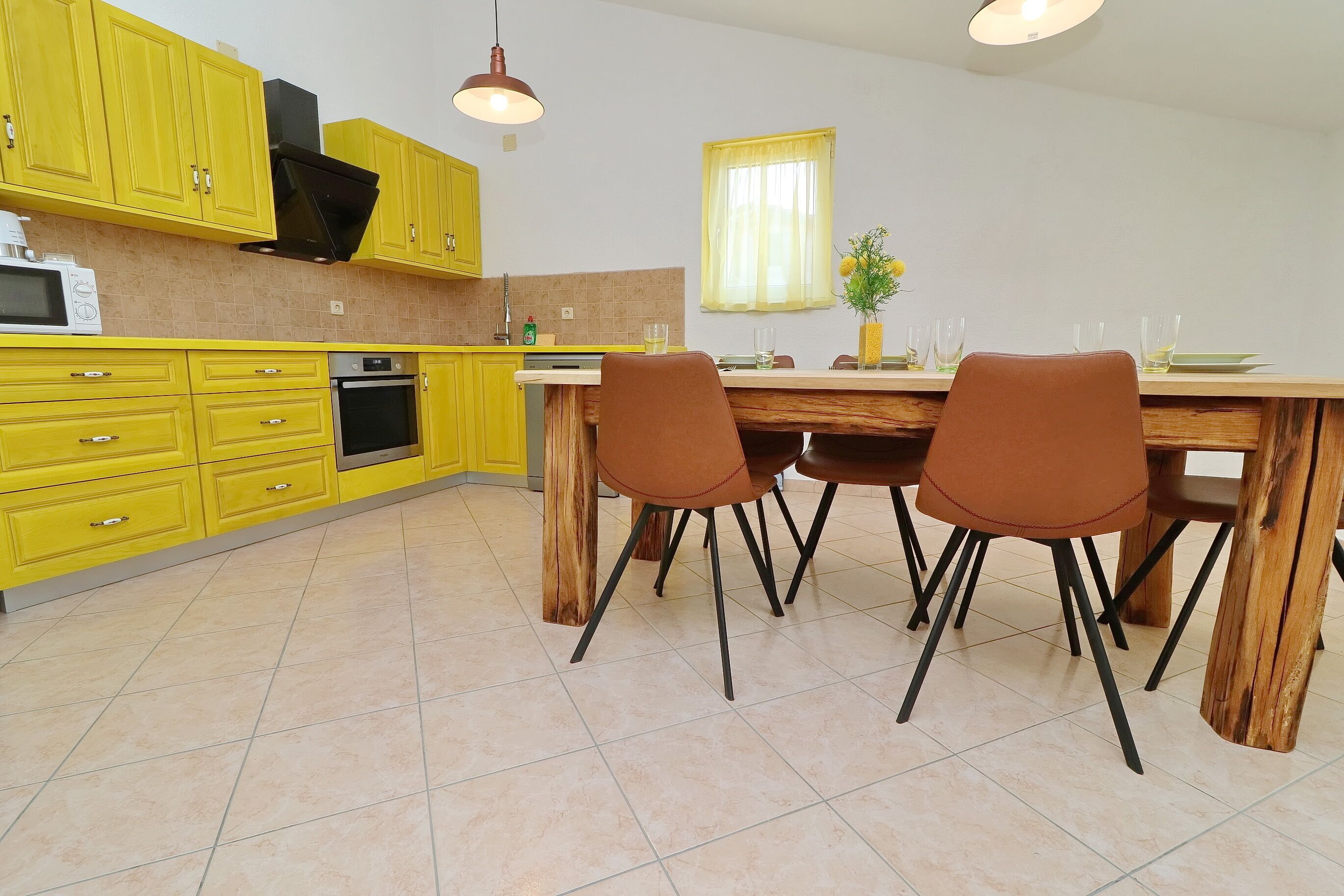 A kitchen with yellow cabinets, a wooden dining table, and brown chairs.