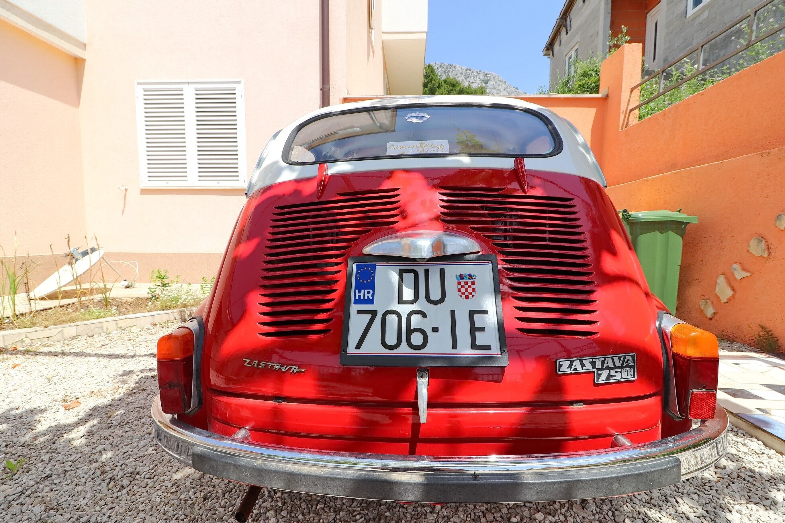 Un'auto rossa d'epoca con targa DU 706 IE parcheggiata su un fondo sterrato.