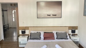 A hotel room with a large bed, two bedside tables, a nightstand, a wall-mounted picture, and a hallway leading to another room. - Apartments Mavi - Studio Apartment with Terrace and City View (Dubrovnik)
