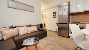 A modern living room with a sofa, a coffee table with a magazine and remote, and a kitchen area with a refrigerator and cabinets. - Apartment Boris (ST) - Two Bedroom Apartment with Terrace and Jacuzzi (Trogir)