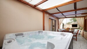 A hot tub in a covered outdoor area with wooden beams, a table with chairs, and a stone wall in the background. - Apartment Boris (ST) - Two Bedroom Apartment with Terrace and Jacuzzi (Trogir)