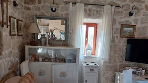 A cozy room with a stone wall, a bed, a dresser, a TV, and a window with curtains.