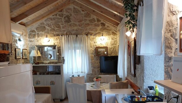A cozy kitchen and dining area with stone walls, wooden beams, and a tiled floor.