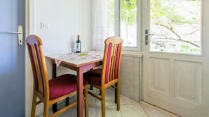 Et spiseområde med et bord, to stole, en vinflaske og et vindue med udsigt til træer.
