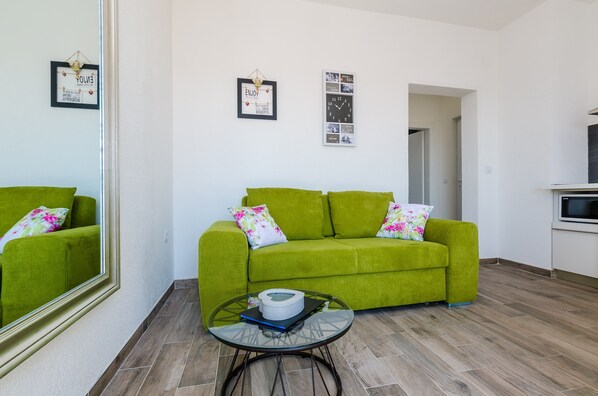 A living room with a green sofa, a glass coffee table, and a large mirror.