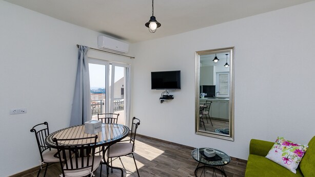Una habitación con una mesa de comedor, sillas, un sofá verde, un televisor y un espejo grande.