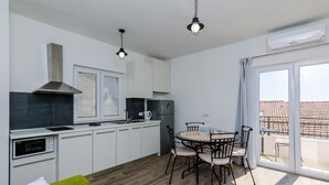 Una cocina compacta con armarios blancos, un microondas integrado y una estufa. Hay una zona de comedor con una mesa redonda y sillas, y un sofá verde.