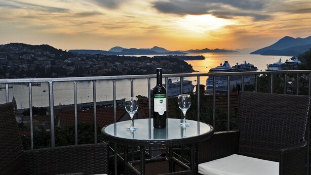 Un balcon avec une table dressée pour deux personnes, offrant une vue sur une étendue d’eau et des montagnes lointaines.