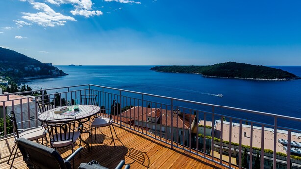 A wooden deck with a round table and chairs, overlooking a coastal view with a clear sky and calm sea. - Amorino of Dubrovnik Apartment - Two Bedroom Apartment with Terrace and Sea View (Apartment Ruzmarin) (Dubrovnik)