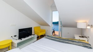 A modern hotel room with a bed, a TV, a yellow chair, and a balcony with a view. - Amorino of Dubrovnik Apartment - Two Bedroom Apartment with Terrace and Sea View (Apartment Ruzmarin) (Dubrovnik)