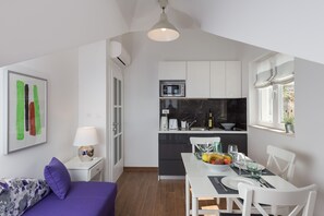 Un espacio habitable compacto con comedor, kitchenette y una cama con almohada morada.