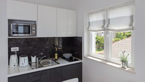 A modern kitchen with a built-in microwave, a sink, a wine bottle, and a potted plant by the window. - Amorino of Dubrovnik Apartment - Two Bedroom Apartment with Terrace and Sea View (Apartment Ruzmarin) (Dubrovnik)