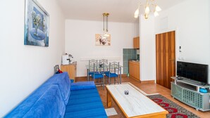 A compact living space with a blue sofa, a dining table, a TV, and a kitchenette. - Apartments Peco - Studio Apartment with Balcony and Sea View (Mokosica)