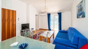 A modern living room with a blue sofa, a glass coffee table, and a TV. - Apartments Peco - Studio Apartment with Balcony and Sea View (Mokosica)