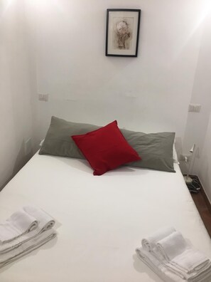 Una cama bien hecha con almohadas blancas y verdes, una obra de arte enmarcada encima y toallas dobladas a un lado.