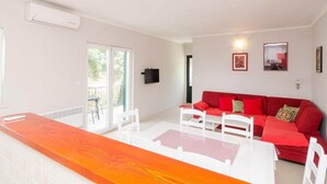 A bright living room with a red sofa, white chairs, and a glass-top table.