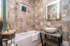Ein Badezimmer mit einer weißen Badewanne, einem Waschbecken und einer gefliesten Wand mit geometrischem Muster.