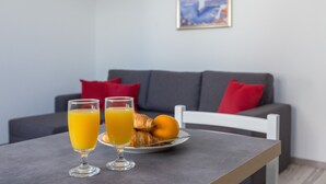 Una mesa de desayuno con dos vasos de zumo de naranja y un plato de cruasanes y una naranja.
