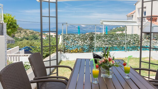 Un espacio de comedor al aire libre con sillas de mimbre y una mesa, con vistas a una piscina y un paisaje montañoso.