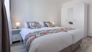 Un dormitorio con cama, mesitas de noche, armario y una mesita de noche con lámpara.