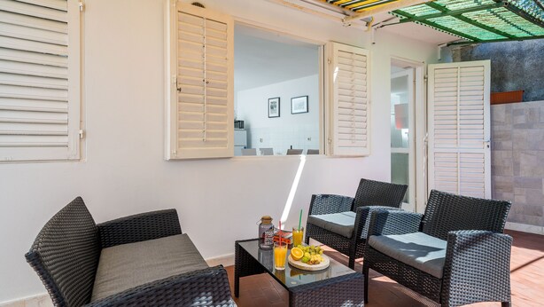 Uma área de estar externa com móveis de vime, uma mesa de vidro e um prato de frutas.