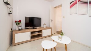 Uma sala de estar moderna com televisão, aparador de madeira, mesa branca e cadeiras.