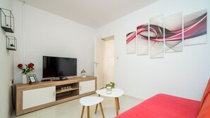 Uma sala de estar moderna com televisão de tela plana, armário de madeira, sofá branco e uma parede com detalhes vermelhos.