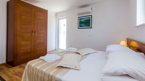 Ein Schlafzimmer mit einem Bett, Kissen, einem Holzschrank, einem Gemälde und einer Klimaanlage.