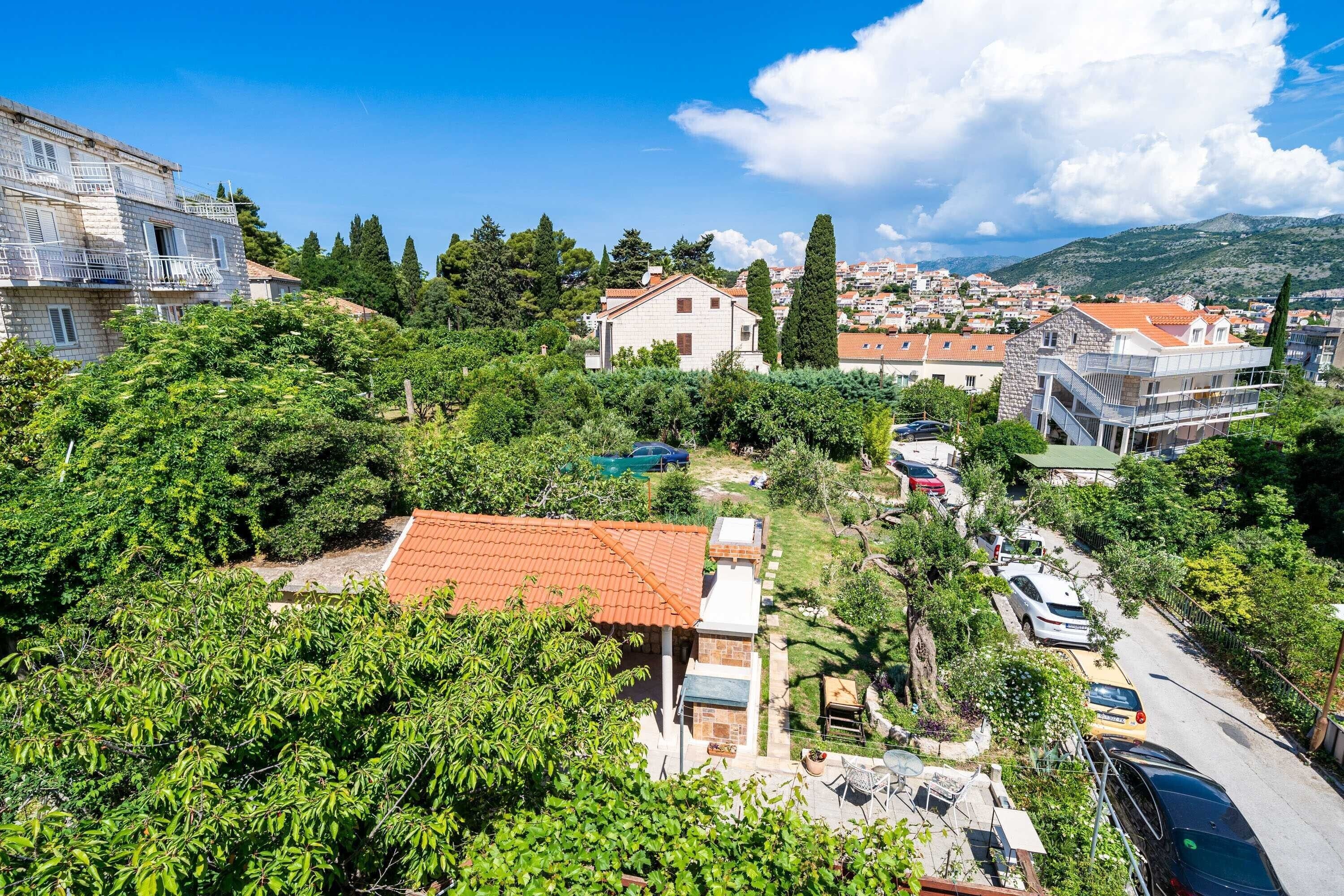 Zona residencial com mistura de edifícios de pedra e modernos, rodeada por vegetação e vista clara para uma cidade ao longe.