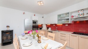 Een moderne keuken met witte kasten, een rode spatwand, en een eethoek voor zes personen met een witte tafelkleed.