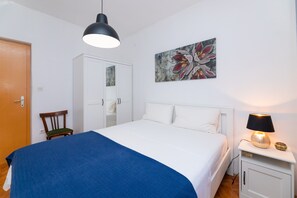 Une chambre à coucher comprenant un lit, une chaise, une armoire, une table de chevet avec une lampe et un tableau accroché au mur.