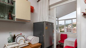 Eine kleine Küche mit einem Kühlschrank, einem Geschirrgestell und einem Fenster mit Blick auf Gebäude.