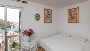 Ein Schlafzimmer mit einem Bett, einem kleinen runden Tisch mit Blumen in einer Vase und zwei gerahmten Bildern an der Wand.