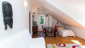 Ein kleiner, gemütlicher Dachzimmer mit schrägen Wänden, einem weißen Sofa, einem Esstisch mit roten Stühlen, einem kleinen Bett und einer Wanddekoration.